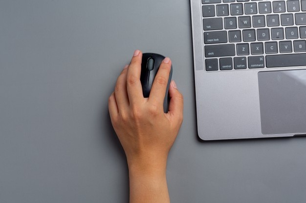 Hand met muis naast laptop.